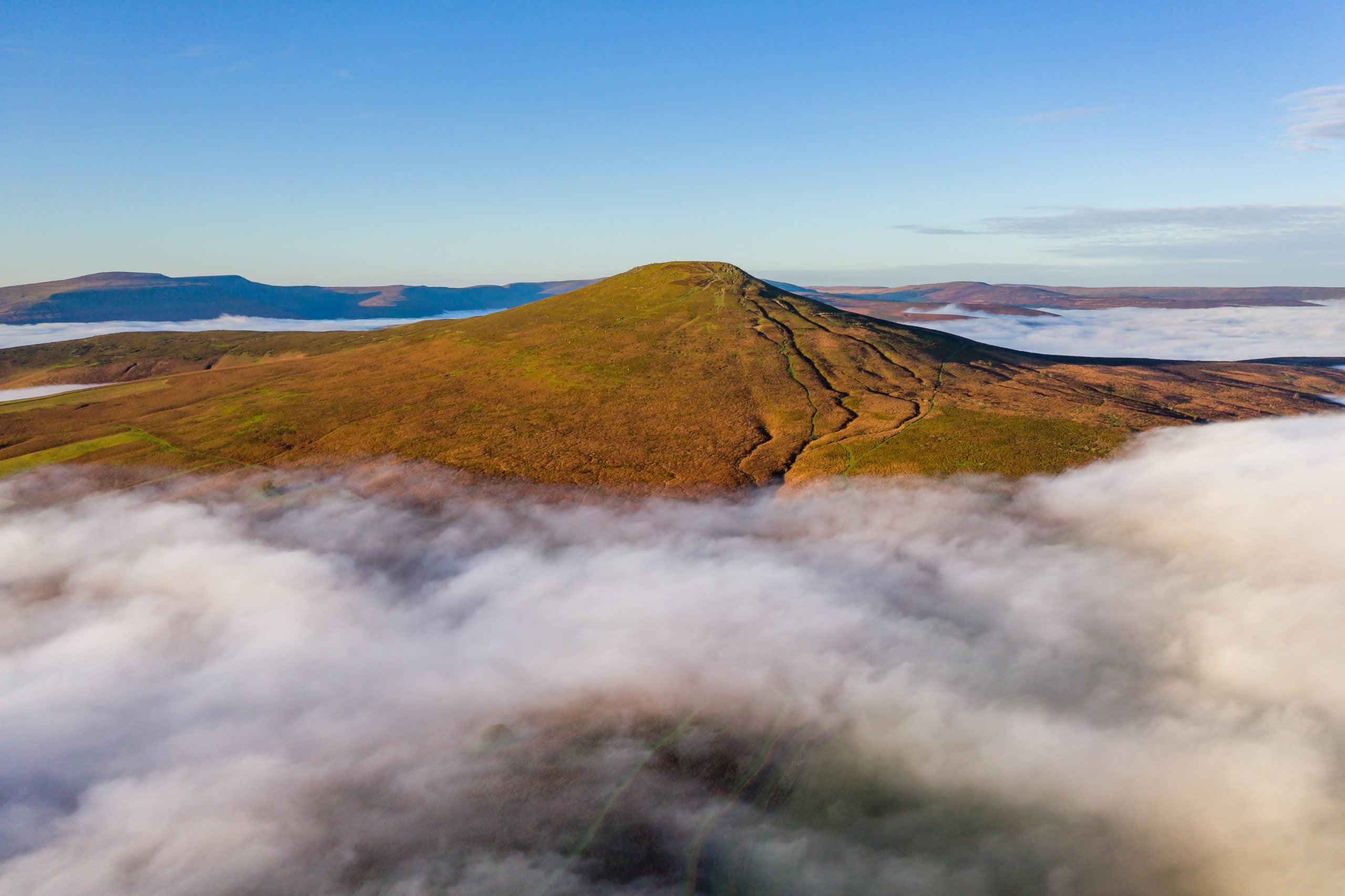Aerial view of a mountain peak rising above a sea of low cloud and fog in the valley below (Sugar Loaf, Wales)